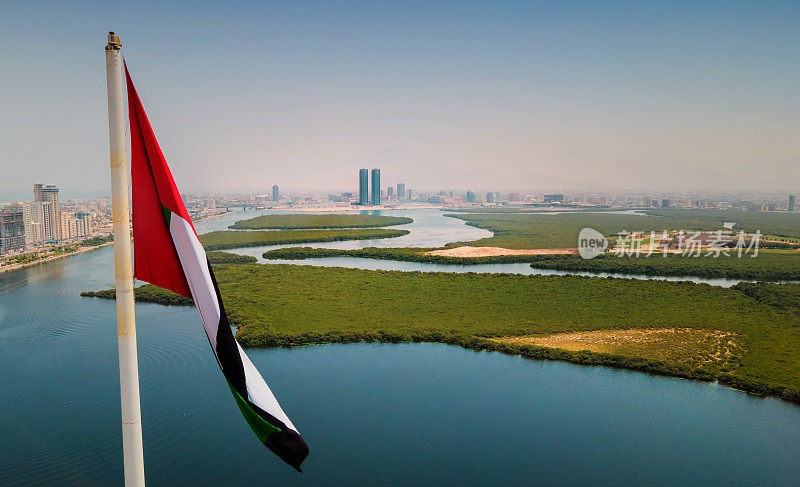 阿联酋国旗和Ras al Khaimah酋长国空中城市景观的标志性天际线上升在阿联酋北部的红树林和小溪